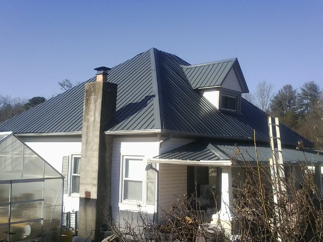 Dark blue standing seam metal roof on a white farmhouse with dormer — Slate & Tile Roof Repair by Roofing Brothers in Colstrip
