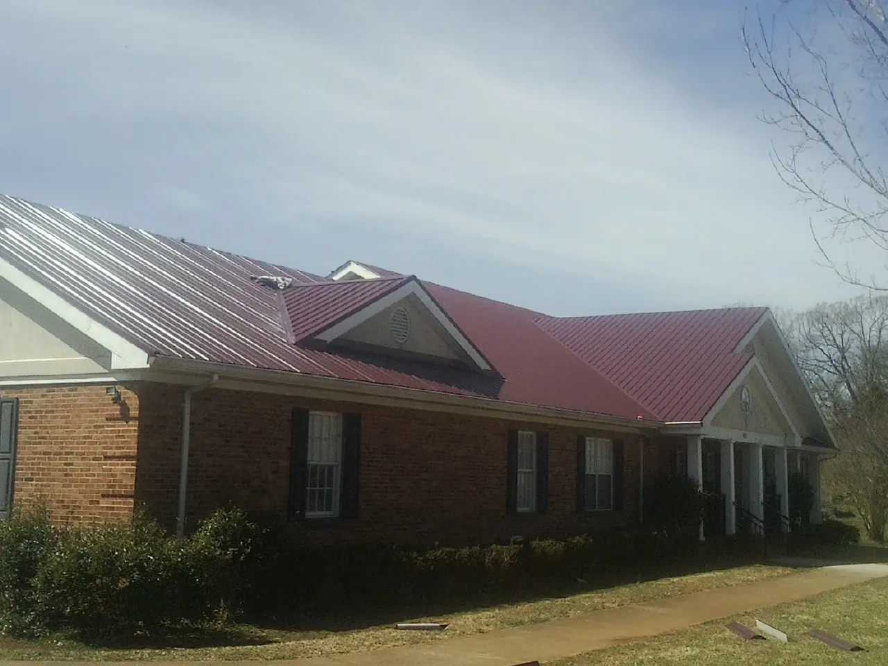 Red metal roof with gabled entries on a long brick building, from a Hail Damage Roof Repair job in Colstrip