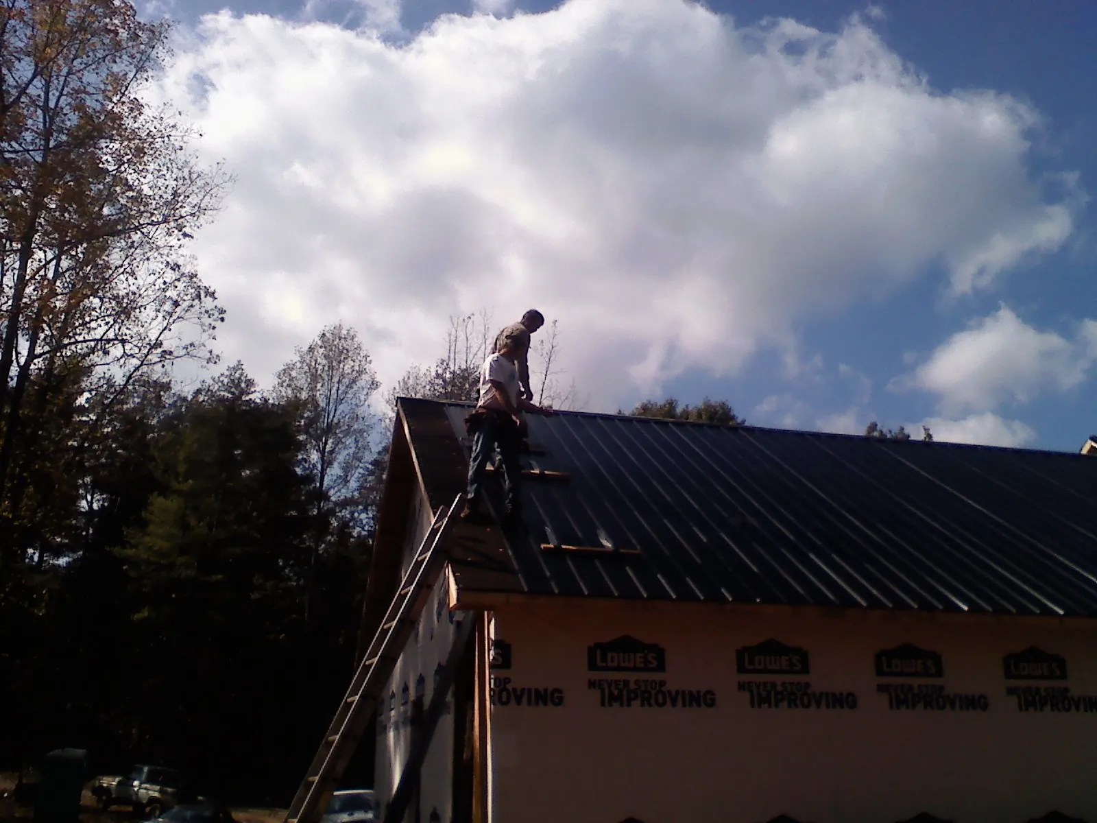 Roofer fastening dark metal panels high against a cloudy sky, from a Roof Inspection job in Colstrip